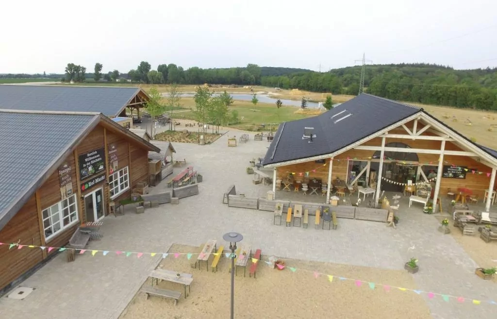 Das Hofgelände des Krewelshof EIFEL mit Hauptgebäuden und See im Hintergrund.